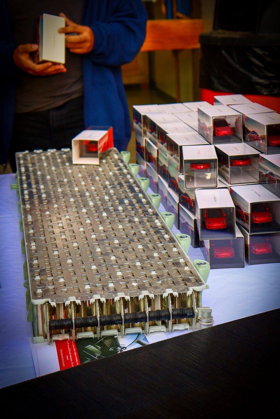 Student holding a miniature Tesla vehicle standing next to a Tesla battery cell module at the 9th Annual Fernley STEM Festival (Nevada, March 3, 2022)